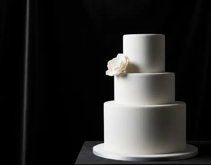 Elegant minimalist white cake with soft petals and dramatic black cinematic background – Blue Heaven Cake Shop in Bhopal