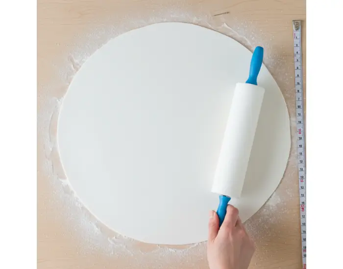 Rolling Out Fondant Evenly for Cake Covering – Step 4 Evenly rolled fondant sheet on a dusted surface, ready to be lifted and placed on the cake