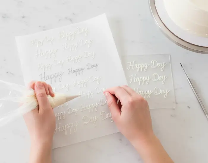 hands piping “Happy Day” practice letters on parchment paper